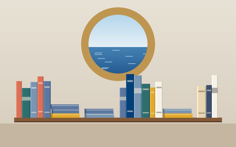 رفٌّ من الكتب تحت نافذةٍ مستديرة تطلّ على البحر